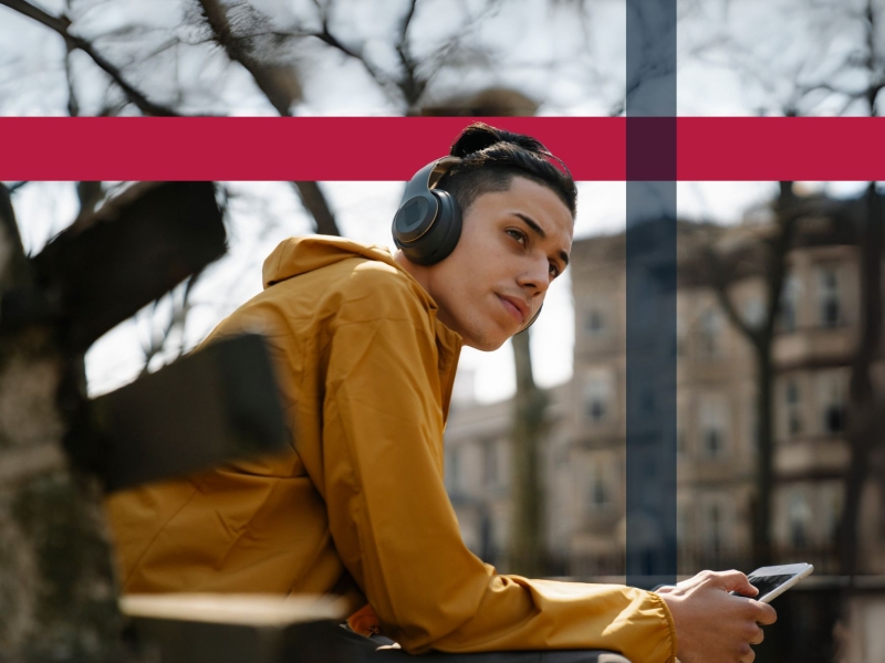 Foto af ung mand, der lytter til lydbog på en bænk